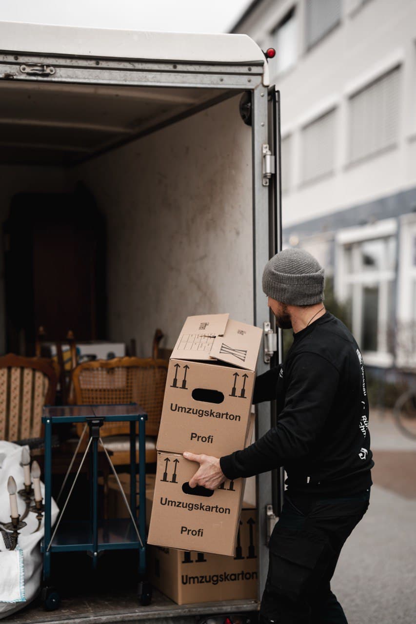 Mitarbeiter trägt Kartons aus der Wohnung zum Transporter